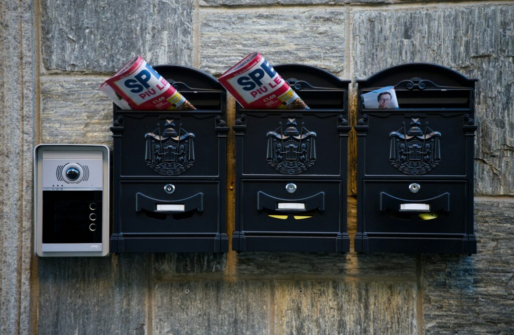 Three mailboxes with mail and a doorbell.