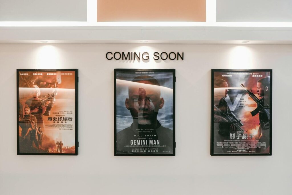 Framed posters of upcoming movies in a cinema hallway under 'Coming Soon' sign.
