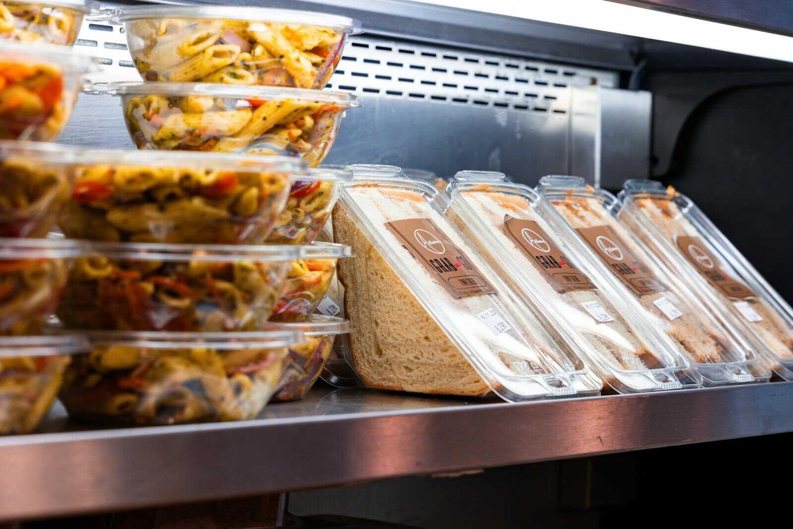 Delicious ready-to-eat pasta salads and sandwiches displayed in a store fridge.