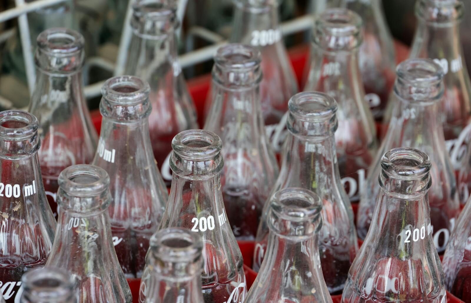 A detailed view of empty glass soda bottles arranged in a red crate, showcasing a repetitive pattern and reflections.