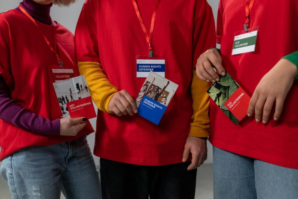 Kako pripremiti materijal za sajam: od flajera do promo proizvoda 4 Volunteers in red shirts holding informational booklets on art and eco volunteering.